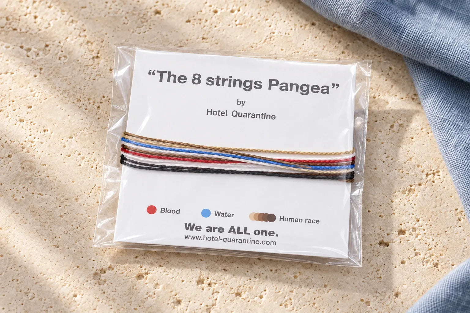 Styled photograph of the Pangea bracelet wrapped around its printed white paper, inside a clear protective sleeve, on pale stone beside blue linen.